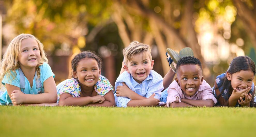 Portrait Of Multi-Cultural Primary Or Elementary School Student Friends Lying On Grass Outdoors